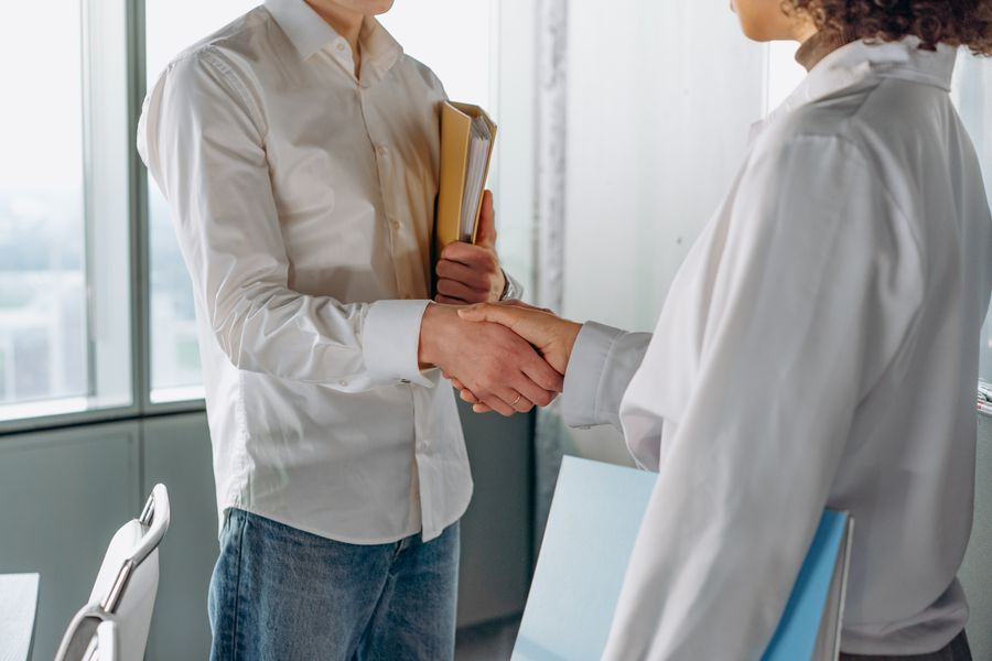 Two people shaking hands over a folder in a bright office